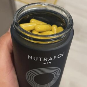 May include: A black bottle of Nutrafol Men hair growth supplement, filled with yellow capsules. The bottle has a silver and white design with the brand name and product information.
