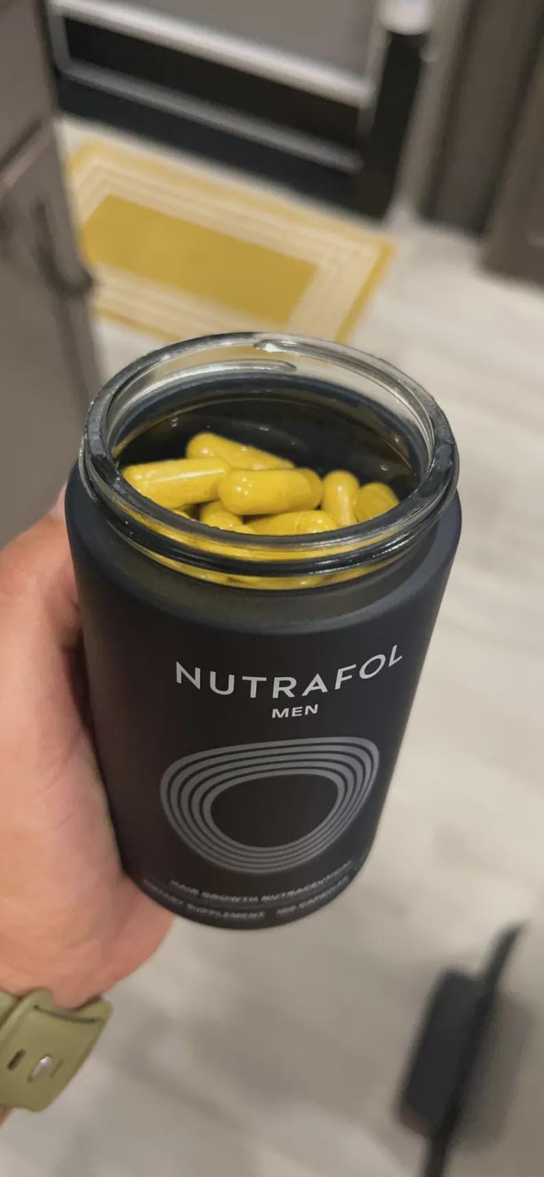 May include: A black bottle of Nutrafol Men hair growth supplement, filled with yellow capsules. The bottle has a silver and white design with the brand name and product information.