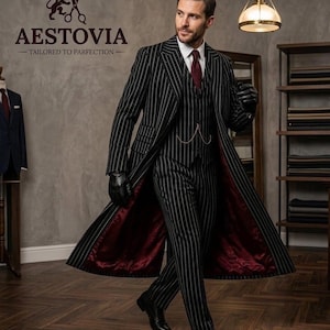 May include: A black pinstripe three-piece suit featuring a long coat with a deep red lining, a white dress shirt, and a dark red tie. The ensemble includes black leather gloves and a gold pocket watch chain. The text AESTOVIA TAILORED TO PARFECTION is visible.