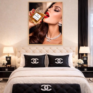 Puede incluir: Un dormitorio lujoso con una obra de arte enmarcada de una mujer bebiendo perfume. La cama tiene almohadas negras y un banco, todos adornados con el logo de Chanel. Mesitas de noche negras con l&aacute;mparas y una ara&ntilde;a completan la opulenta decoraci&oacute;n.