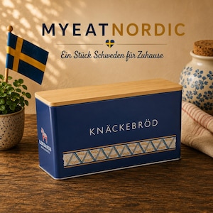 Può includere: Un contenitore rettangolare in metallo blu con coperchio in legno chiaro. La parte anteriore presenta la scritta KNÄCKEBRÖD e un motivo decorativo a spighe di grano. Il lato mostra un piccolo logo rosso a forma di cavallo Dala e la scritta LEKSANDS.