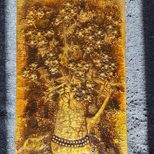 Könnte beinhalten: Ein rechteckiges, geprägtes Metall-Wandbild mit goldener Oberfläche. Das Kunstwerk zeigt eine Vase mit stilisierten Blumen und Beeren. Die Vase hat einen Henkel und ist mit einer Reihe kleiner, runder Akzente verziert. Der Hintergrund hat ein strukturiertes Aussehen.