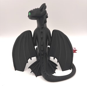 May include: A black dragon figurine with large wings and a long tail. The dragon has green eyes and is posed with its wings spread. The figurine is made of a smooth material and sits on a white surface.