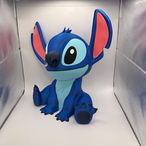 May include: A blue Stitch figurine with large ears, a black nose, and large eyes. The figurine is sitting with its arms and legs outstretched. The inside of the ears are pink. The figurine is a popular character from the animated movie Lilo & Stitch.