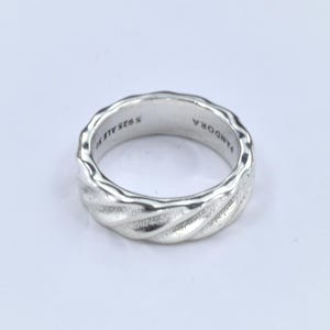 May include: A silver ring with a textured, twisted rope design. The ring is stamped with "S925 ALE" and "PANDORA". The ring is a size 7.