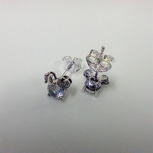 May include: A pair of silver-toned stud earrings. Each earring features a light blue, oval-shaped gemstone set within a decorative frame. The earrings have a post and butterfly backing for secure wear.