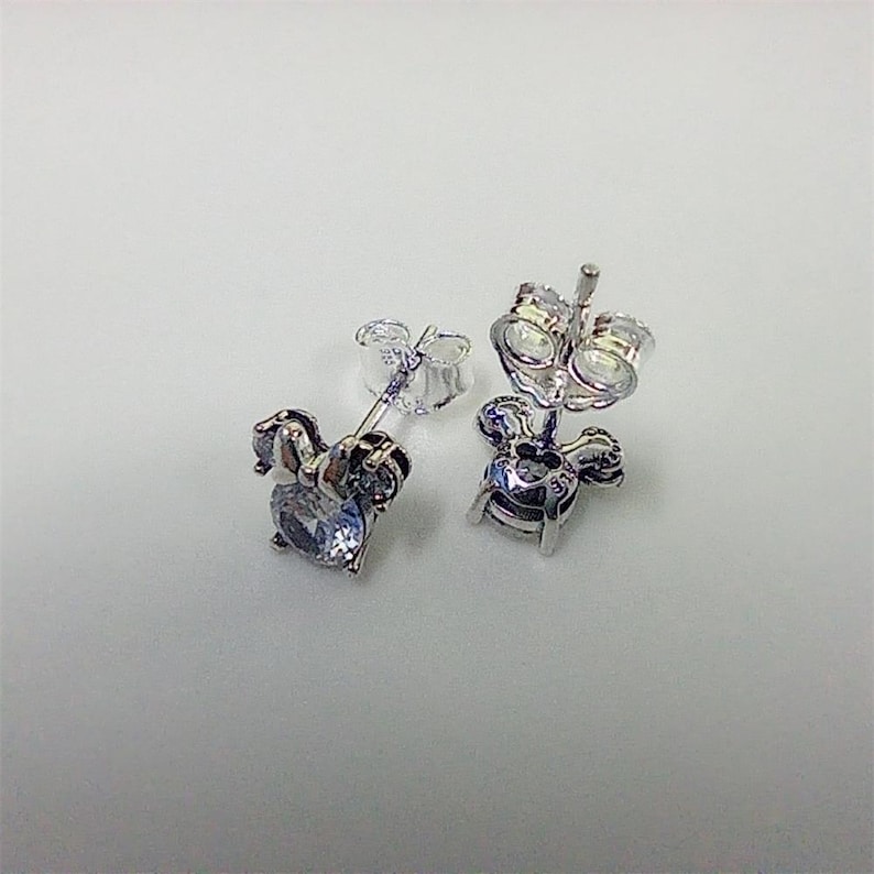 May include: A pair of silver-toned stud earrings. Each earring features a light blue, oval-shaped gemstone set within a decorative frame. The earrings have a post and butterfly backing for secure wear.