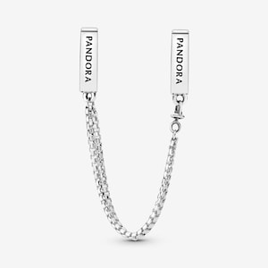 Può includere: Catena di sicurezza per bracciale Pandora in argento. La catena presenta due barre rettangolari con la scritta "PANDORA" stampata. La catena è composta da piccole maglie quadrate e collega le due barre. Un'estremità ha una chiusura.