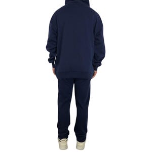 May include: Navy blue hoodie and matching sweatpants set. The hoodie has a drawstring hood and long sleeves. The sweatpants have a straight leg design. The person is wearing white sneakers. The set is made of a soft, comfortable material.