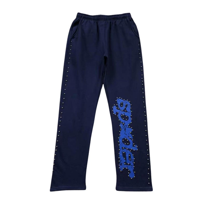 May include: Navy blue sweatpants with a drawstring waist and pockets. The left leg features the word "Border" in blue, outlined with silver studs. Silver studs also line the outer seams of both legs.