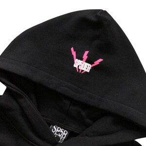 May include: Black hoodie with a hood. The hood features a pink lightning bolt design with the word "SP5DER" in white. The lower part of the hoodie has the text "SP5B" in white.