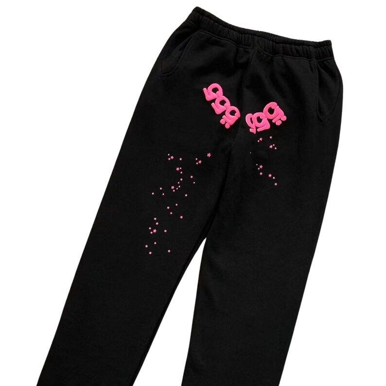 May include: Black sweatpants with a pink graphic design. The design includes the number "999" in a stylized font, repeated twice, and scattered pink star-shaped accents. The sweatpants have a drawstring waistband and pockets.