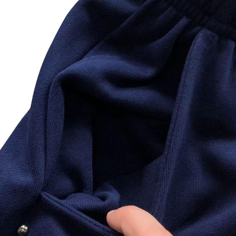 May include: Close-up of navy blue sweatpants with a visible pocket and a drawstring waistband. The fabric appears to be a soft knit material. The image shows a portion of the pants, highlighting the texture and color.