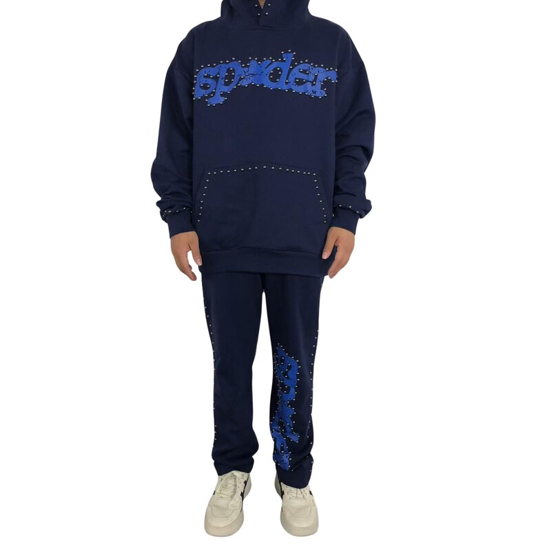 May include: Navy blue hoodie and sweatpants set. The hoodie features the word "spyder" in blue, studded with silver accents. The sweatpants have the same design on the left leg. The set includes a hood and a front pocket.
