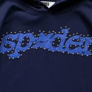 May include: Navy blue hoodie with the word "Spyder" in a distressed blue font, studded with silver-colored embellishments. The hoodie has a drawstring hood and is made of a soft material.