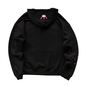 May include: Black hooded sweatshirt with pink star accents on the left sleeve and a pink graphic on the hood. The sweatshirt is a casual garment, suitable for everyday wear.
