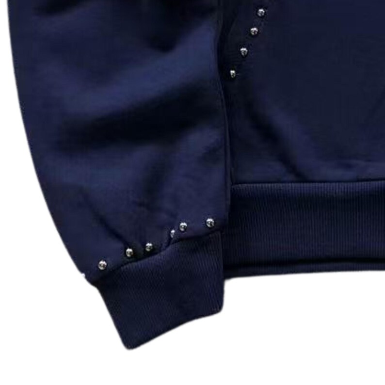 May include: Navy blue sweatshirt with silver-colored stud embellishments along the sleeve and cuff. The cuff and bottom hem are ribbed. The sweatshirt is a solid color.