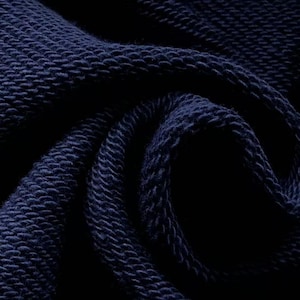 May include: Close-up of a navy blue knitted fabric. The texture is visible, with a pattern of raised, looped stitches. The fabric is tightly woven, creating a dense and durable material. The dark blue color is consistent throughout the image.