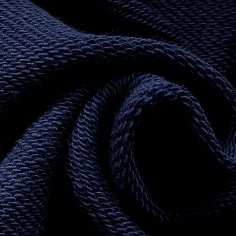 May include: Close-up of a navy blue knitted fabric. The texture is visible, with a pattern of raised, looped stitches. The fabric is tightly woven, creating a dense and durable material. The dark blue color is consistent throughout the image.