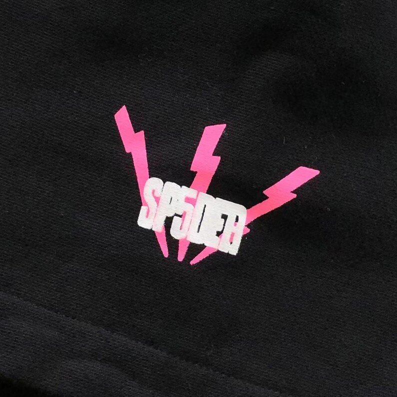 May include: Black fabric with a pink and white graphic. The graphic features the word "SP5DER" in white block letters, framed by three pink lightning bolts.