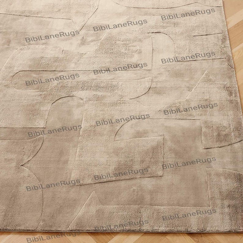 May include: A beige area rug with an abstract design. The rug features raised geometric shapes in varying sizes and textures. The words "BibiLaneRugs" are printed across the rug in multiple places. The rug is placed on a wooden floor.