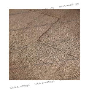 May include: Close-up of a textured, beige rug with a geometric design. The rug has a soft, plush appearance and a subtle pattern created by the weave. The edges of the rug are slightly darker, creating a border effect. The rug is a neutral color.