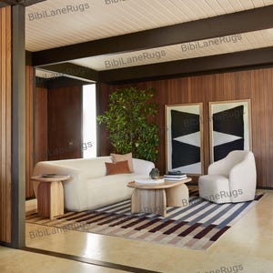 May include: A contemporary living room with a cream sofa, armchair, and a striped rug in grey, brown, and burgundy tones. Two framed abstract artworks adorn the wood-panelled wall. The room features wooden side tables and a coffee table. The room has a modern design.