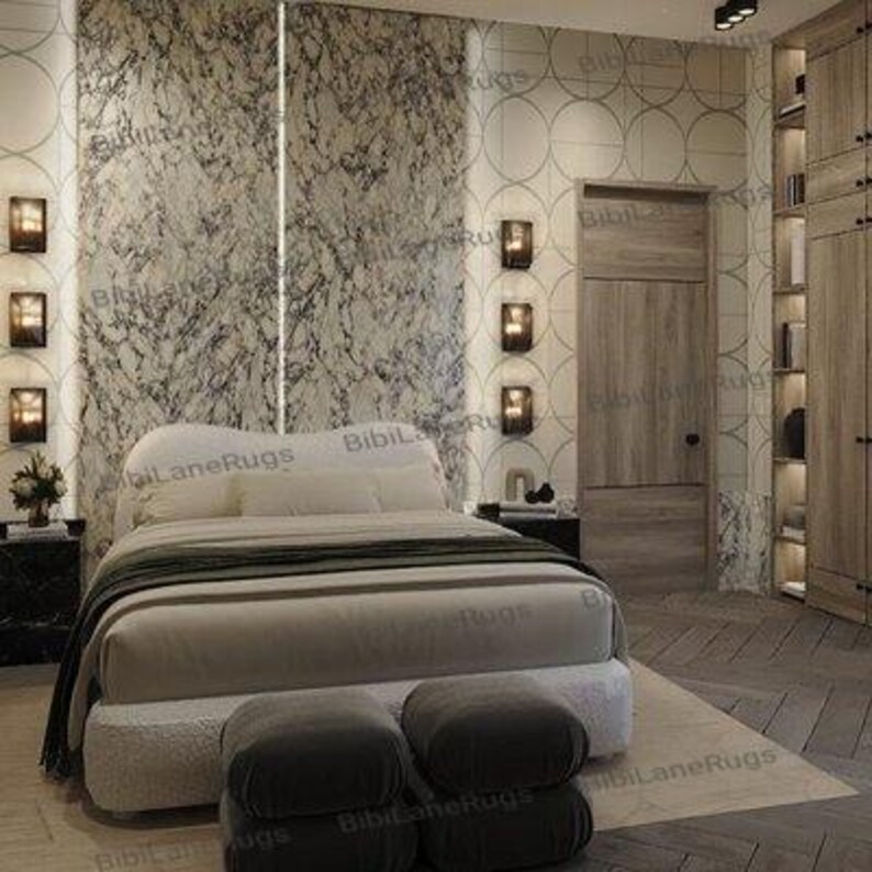 May include: A bedroom scene featuring a large bed with a cream-colored headboard and bedding. Two dark gray ottomans sit at the foot of the bed. The room has marble-patterned wall panels and a wooden door. Wall sconces provide ambient lighting.