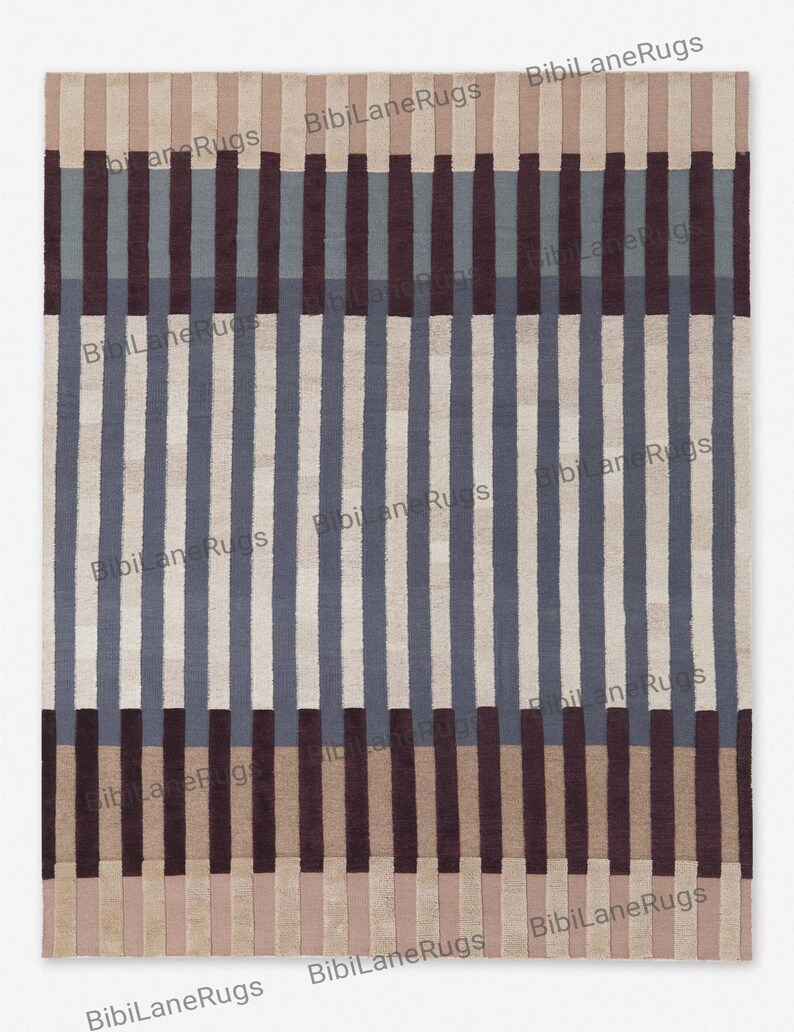 May include: A rectangular rug featuring a striped pattern in blue, brown, and beige. Vertical stripes alternate in colour, creating a geometric design. The rug has the text "BibiLaneRugs" repeated across the image.