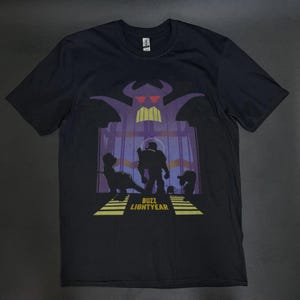 K&ouml;nnte beinhalten: Schwarzes T-Shirt mit einer Grafik von Buzz Lightyear und Zurg aus Toy Story. Das Design umfasst Silhouetten von Charakteren und den Text "Buzz Lightyear" in Gelb. Der Hintergrund zeigt eine lila und gelbe Struktur.