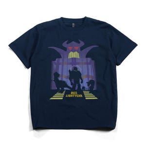 K&ouml;nnte beinhalten: Marineblaues T-Shirt mit einer Grafik aus dem Film Toy Story. Das Design zeigt Silhouetten von Charakteren und den Text "BUZZ LIGHTYEAR" in Gelb. Die Grafik ist vor einem lila und gelben Hintergrund platziert.
