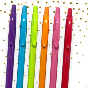 May include: Six colorful pens in purple, blue, green, orange, pink, and red are arranged diagonally against a white background with gold polka dots. Each pen has a matching colored clip and tip.