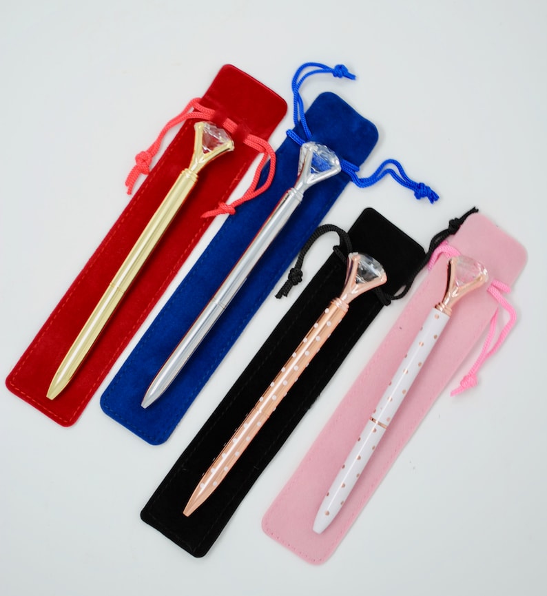 May include: Five diamond-shaped pens in velvet pouches. The pens are gold, silver, rose gold, and white with black polka dots. The pouches are red, blue, black, and pink.
