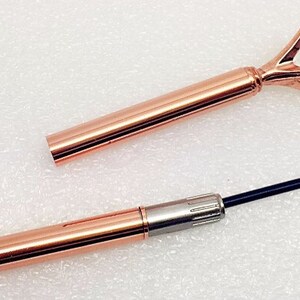 May include: A rose gold pen with a clear diamond-shaped top. The pen is extended to show the black ink cartridge.
