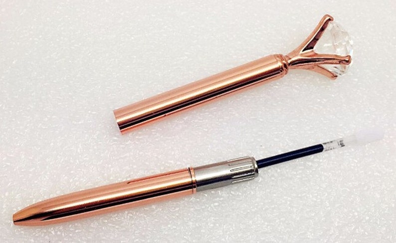 May include: A rose gold pen with a clear diamond-shaped top. The pen is extended to show the black ink cartridge.