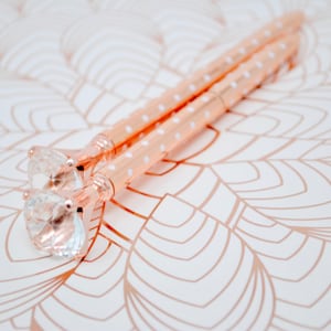 May include: Two rose gold pens with white polka dots and clear crystal tops.