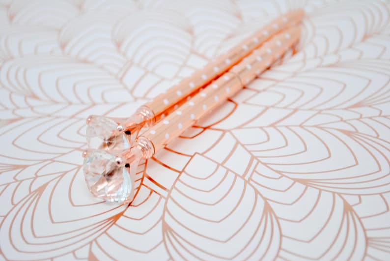 May include: Two rose gold pens with white polka dots and clear crystal tops.