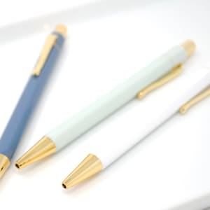 May include: Three pens with gold accents. One is blue, one is light green, and one is white.