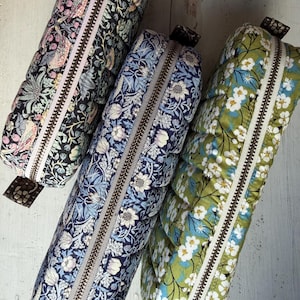 May include: Three rectangular quilted pouches with metal zips. The left pouch features a black background with colourful birds and floral patterns. The middle pouch has a blue floral print. The right pouch is green with white flowers.