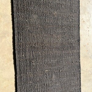 May include: A rectangular, dark gray woven rug. The rug has a textured surface and is made of a natural fiber. The words "Mohan Exports" are printed in white at the bottom of the rug. This rug is suitable for home decor.