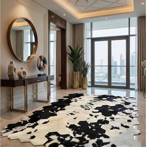 Può includere: Un interno lussuoso con un tappeto in pelle di mucca bianco e nero con un motivo geometrico. Il tappeto è posizionato su un pavimento in marmo, completato da uno specchio con cornice dorata e una consolle in legno scuro. Le piante alte in vasi dorati aggiungono un tocco di verde.