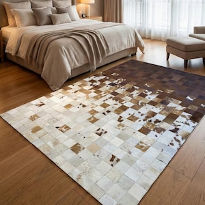 Puede incluir: Una alfombra rectangular de piel de vaca con un patrón a cuadros en tonos marrones, beige y blancos. La alfombra está colocada sobre un suelo de madera en un dormitorio, con una cama y otros muebles visibles en el fondo.