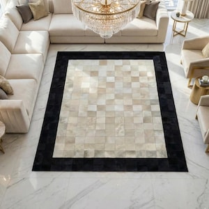 May include: A large, rectangular area rug with a checkerboard pattern in shades of beige and cream, framed by a wide black border. The rug is placed on a marble floor, and is surrounded by beige furniture.