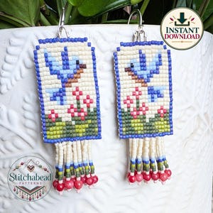 May include: A pair of rectangular beaded earrings featuring a light blue bird design on a cream background with green foliage and pink flowers. The earrings have a blue beaded border and a fringe bottom with cream, blue, green, and pink beads.
