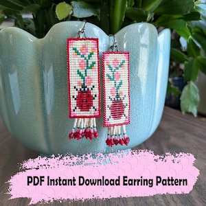 May include: Rectangular earrings with a white background, red border, and a ladybug design. The earrings feature a floral pattern with pink flowers and green stems. The bottom of the earrings have a beaded fringe with red and white beads.