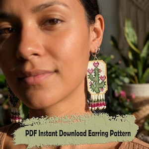 May include: A close-up of a person wearing beaded earrings. The earrings are rectangular with a cactus design in green, pink, and white. The earrings have a fringe of white and pink beads. The text "PDF Instant Download Earring Pattern" is at the bottom.