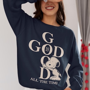 Könnte beinhalten: Marineblaues Sweatshirt mit dem Text "GOD IS GOOD ALL THE TIME" in Creme. Das Design beinhaltet einen Cartoon-Hund. Das Sweatshirt hat lange Ärmel und einen Rundhalsausschnitt.