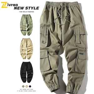 Pode incluir: Calças cargo verde-oliva com vários bolsos e cintura com cordão. A imagem também mostra calças semelhantes em cáqui e preto. O texto "Zivraa NEW STYLE TIDE MALE FASHION" é visível no topo.