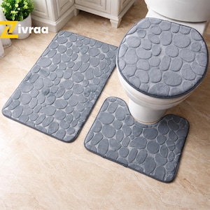 Puede incluir: Un juego de baño de tres piezas en tonos grises, que incluye una alfombra de baño rectangular, una funda para el asiento del inodoro y una alfombra en forma de U. Cada pieza tiene un patrón de guijarros. El conjunto está diseñado para la decoración del baño.