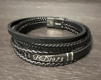 May include: Black leather bracelet with a multi-strand design, including a braided section. The bracelet has a silver clasp with the word "blaze" and a silver plate with the inscription "BD1973".